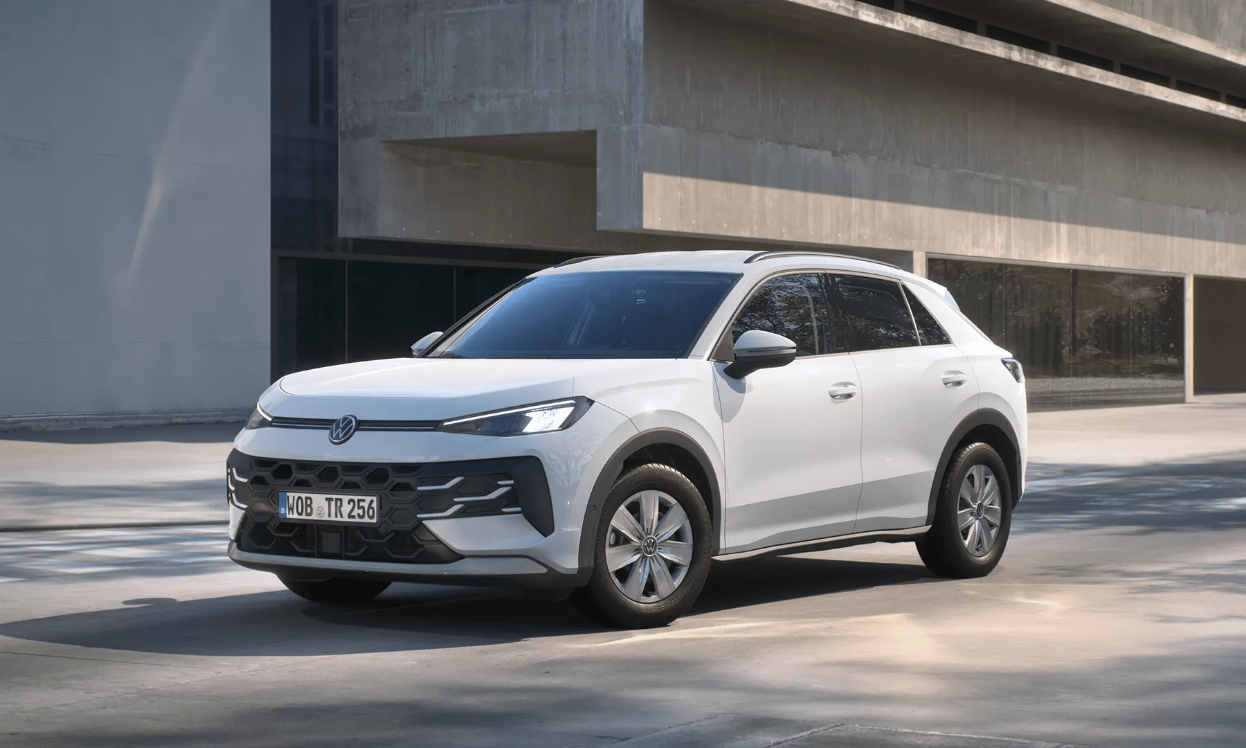 Balts Volkswagen T-Roc Trend stāv modernas ēkas priekšā.