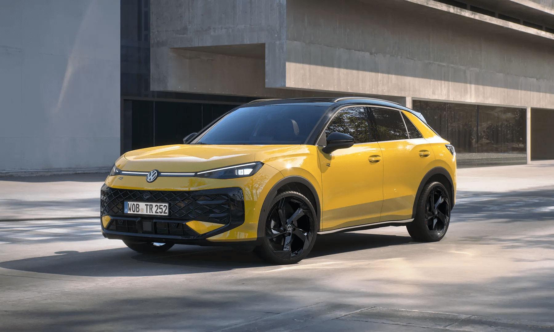 Dzeltens Volkswagen T-Roc R-Line stāv pie ēkas ar melniem diskiem.