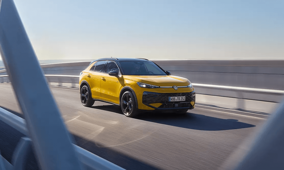 Dzeltens Volkswagen T-Roc brauc pa tiltu saulainā dienā.