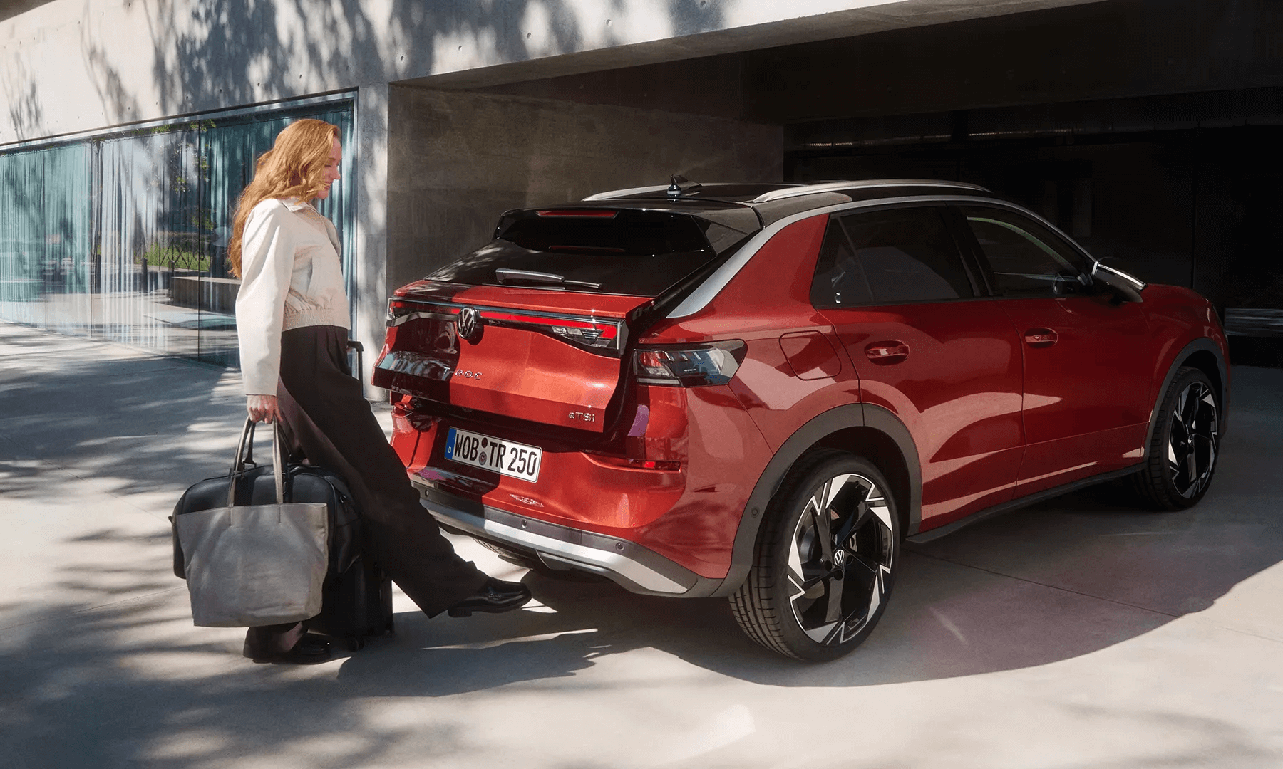 Sieviete ar bagāžu aktivizē sarkana Volkswagen T-Roc bagāžnieku bez roku palīdzības.