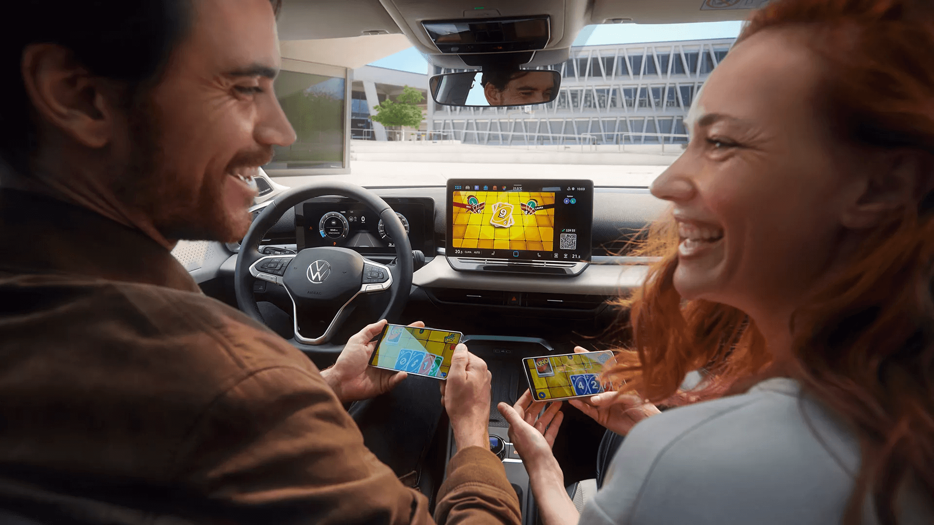 Pāris spēlē spēli savos tālruņos, izmantojot Volkswagen T-Roc ekrānu.