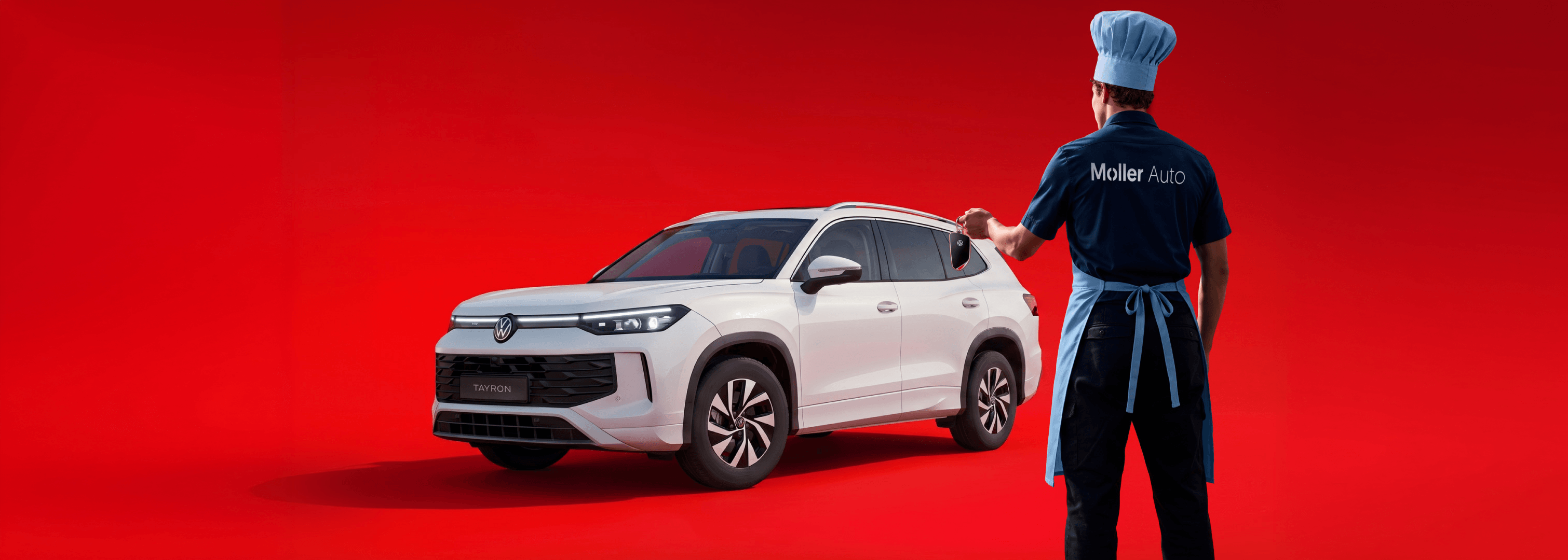 Balts Volkswagen Tayron apvidus auto uz sarkana fona, blakus Möller Auto darbinieks pavāra cepurē un priekšautā, rokā automašīnas atslēga.